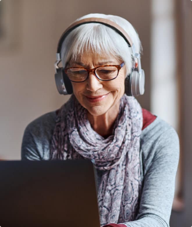 Older woman with headphones smiling and looking at her computer