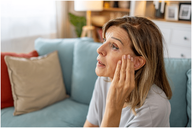 An older woman holds her ear to relieve pain due to her tinnitus symptoms.